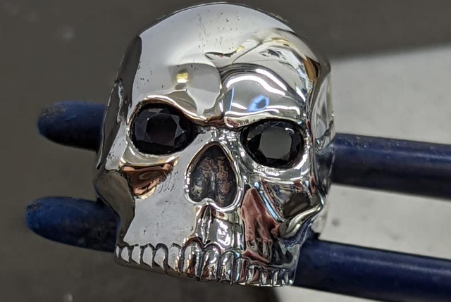 A large skull ring made in silver being held in a pair of jewellers tweezers.